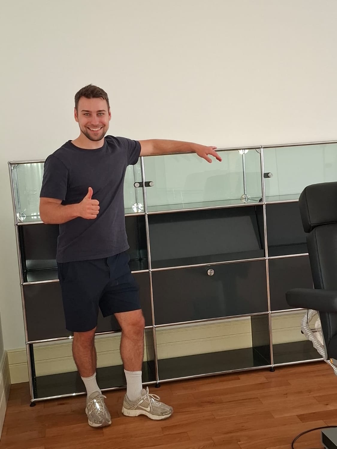 Dr. Marcus Mulica mit Daumen hoch vor dem fertig montierten Highboard mit Glasvitrinen